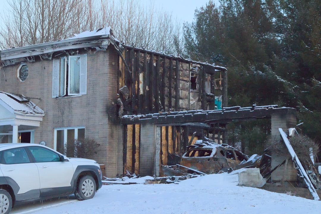 Two story brick house heavily damaged by fire with exposed framing a collapsed roof and a burned out car in a snow covered yard