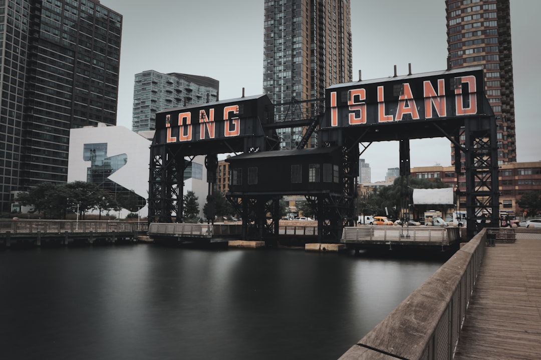Industrial drawbridge with the words long island in orange letters over a calm river city skyscrapers in the background