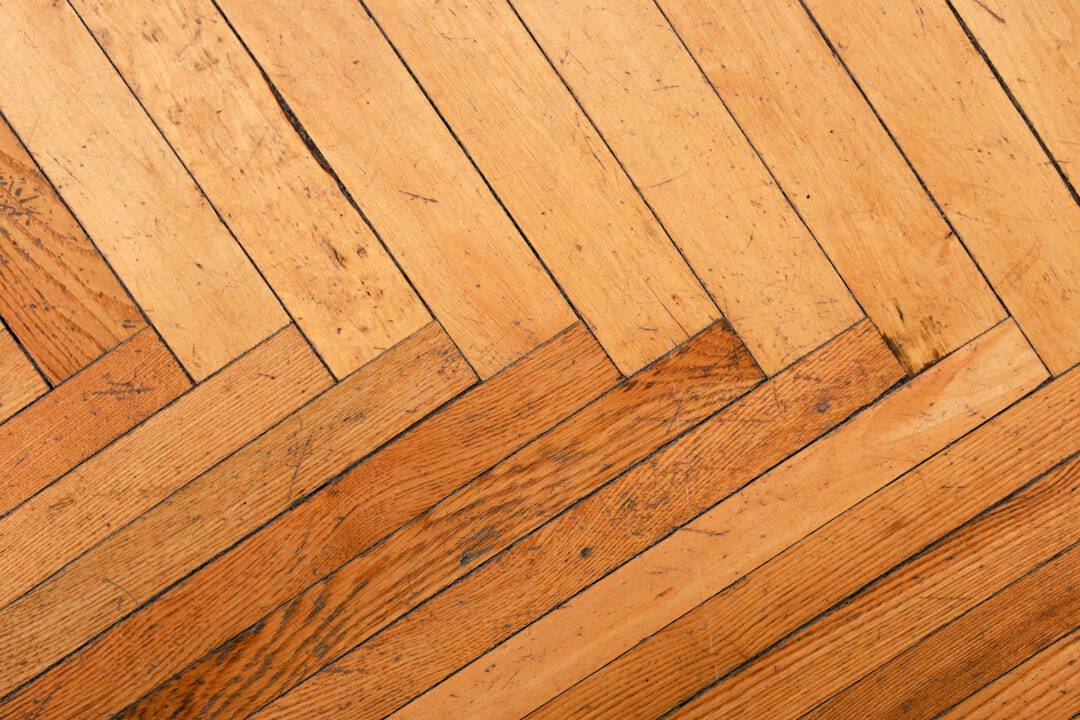 Diagonal wooden floor with warm brown planks arranged in a herringbone pattern, showing grain and wear marks.