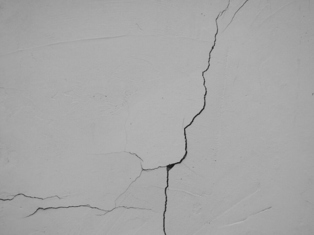 Cracked gray concrete wall with a prominent vertical fissure running from top to bottom, showing age and damage.