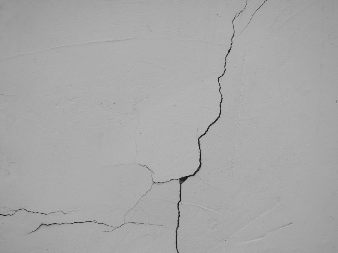 Cracked gray concrete wall with a prominent vertical fissure running from top to bottom, showing age and damage.