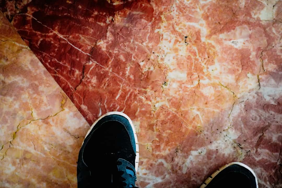 Top-down view of black sneakers standing on a red, veined marble floor