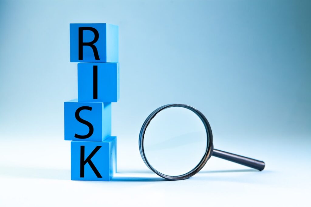 Blue cubes stacked to spell 'RISK' with a magnifying glass beside them, symbolizing risk assessment/analysis.